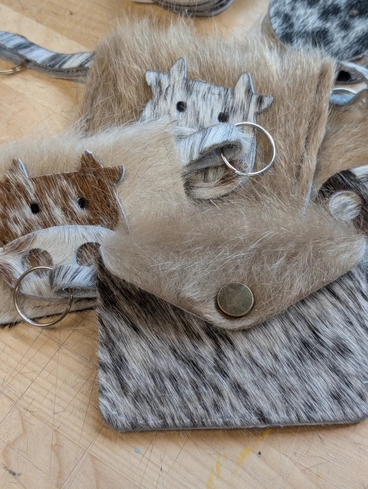 A rustic cowhide keychain card holder made from natural hide with a silver metal ring and button closure