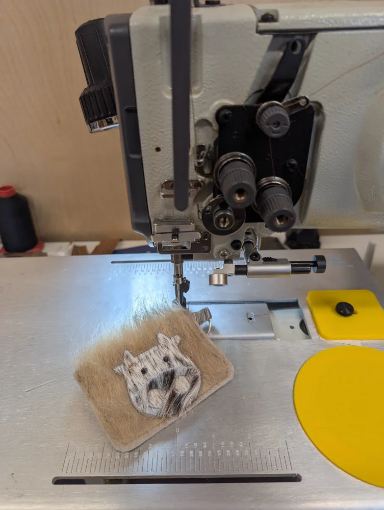 Beige fuzzy cowhide keychain card holder with a stitched white and gray cat face patch design