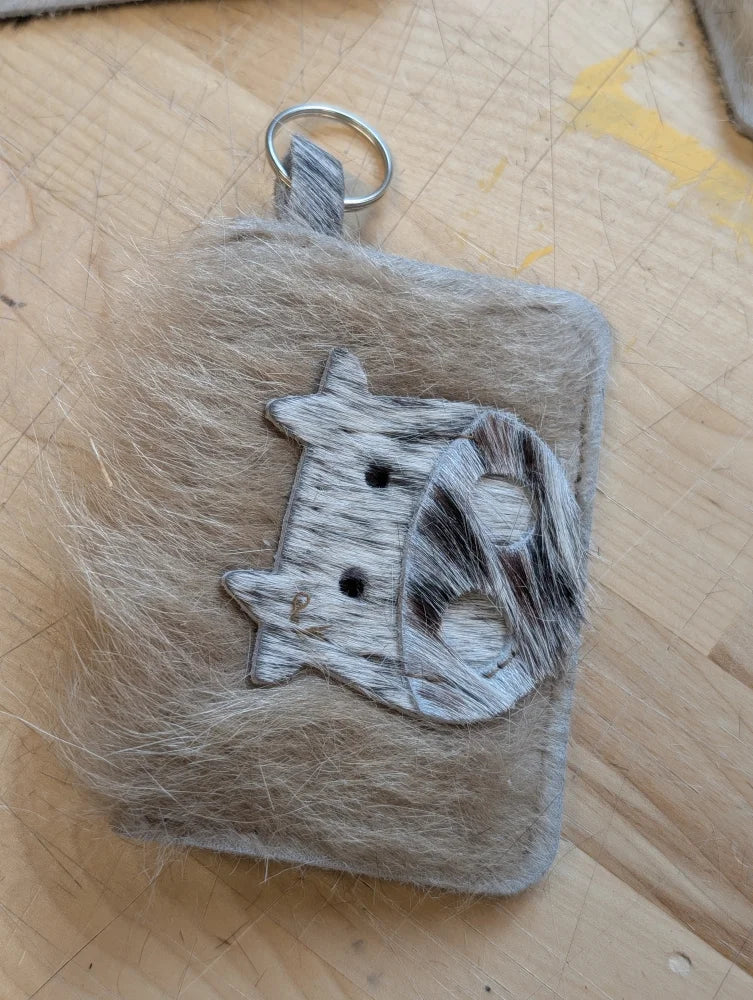 Furry gray keychain card holder with a black and white cow face appliqué made of textured material