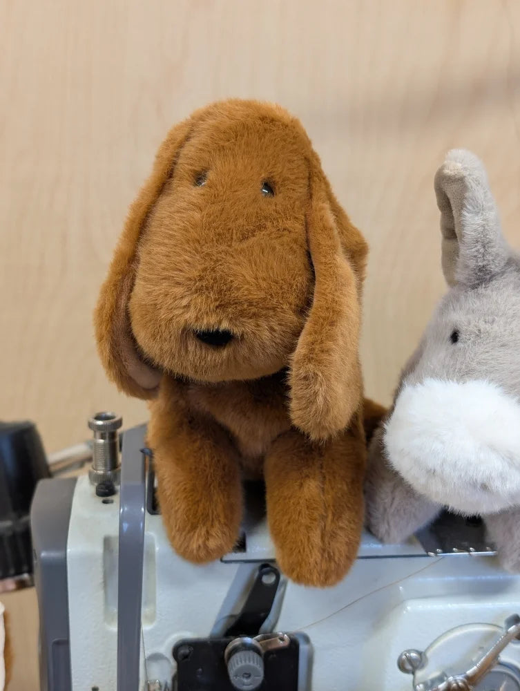 A plush brown dacshund dog with long floppy ears and soft fuzzy texture sitting on a sewing machine
