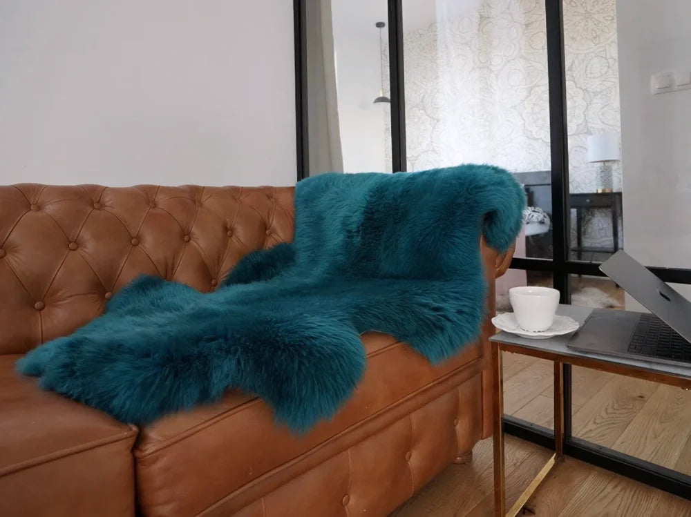 Teal faux fur throw blanket draped over brown leather sofa in dark green aqua merino sheepskin style arriving soon