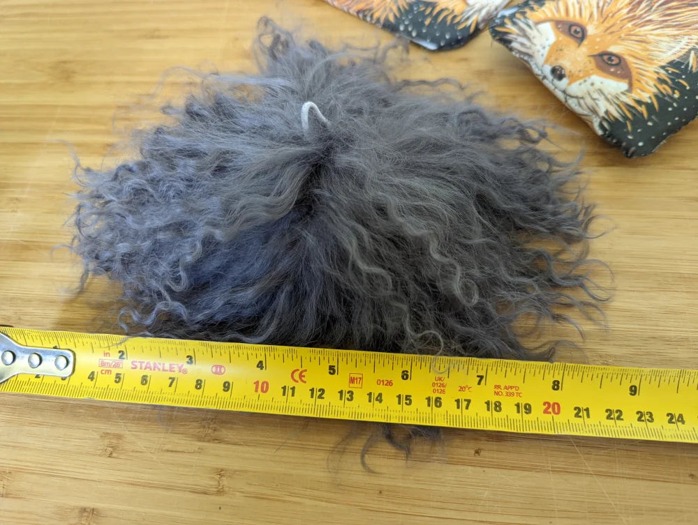 Dark grey sheepskin pom pom ball with fluffy grey texture and white string