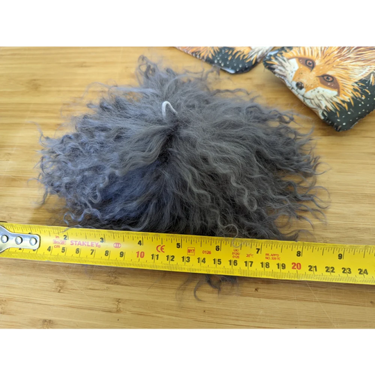 Dark grey sheepskin pom pom ball with fluffy grey texture and white string