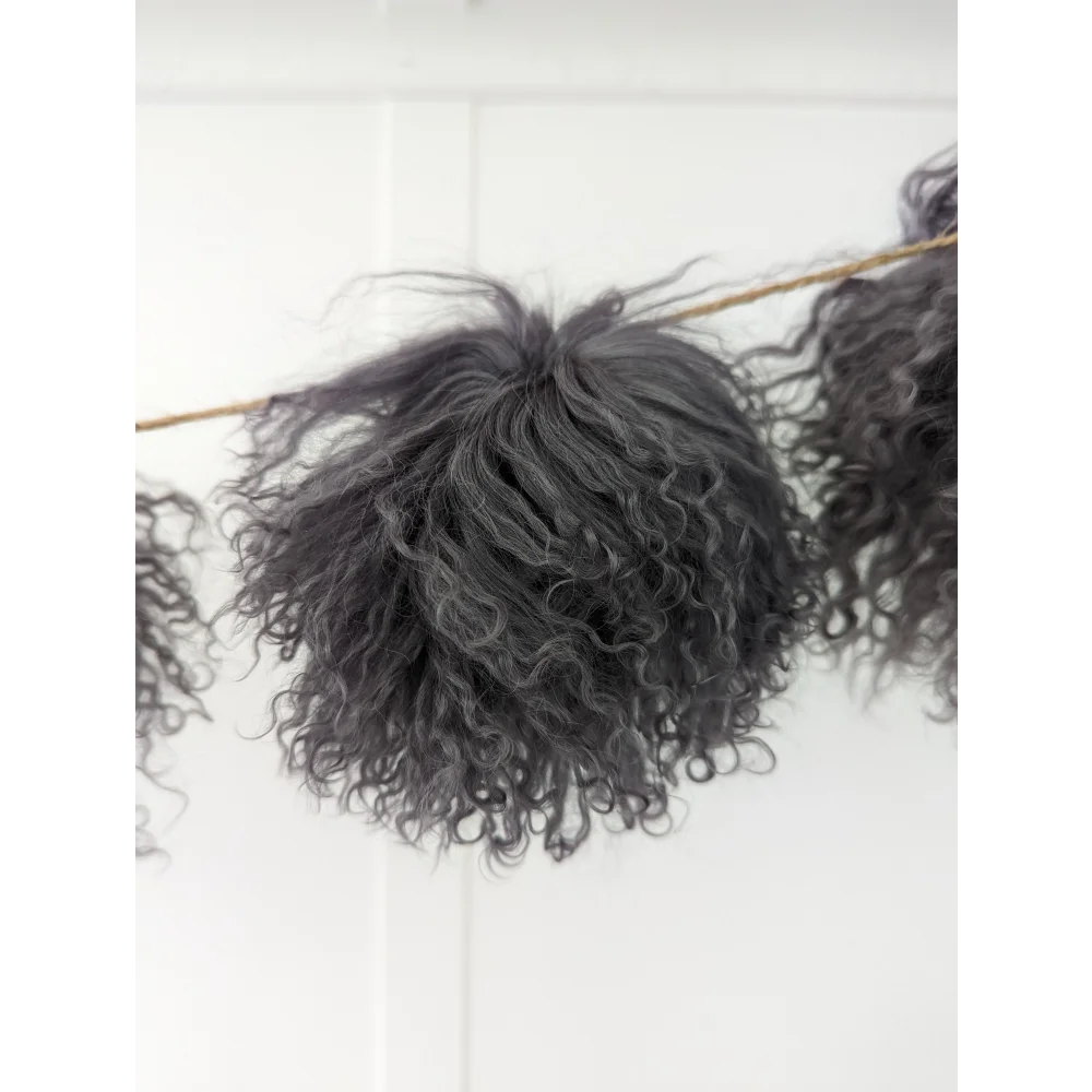 Dark grey sheepskin pom pom with curly black yarn on wooden stick