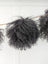 Dark grey sheepskin pom pom with curly black yarn on wooden stick