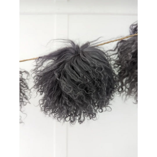 Dark grey sheepskin pom pom with curly black yarn on wooden stick