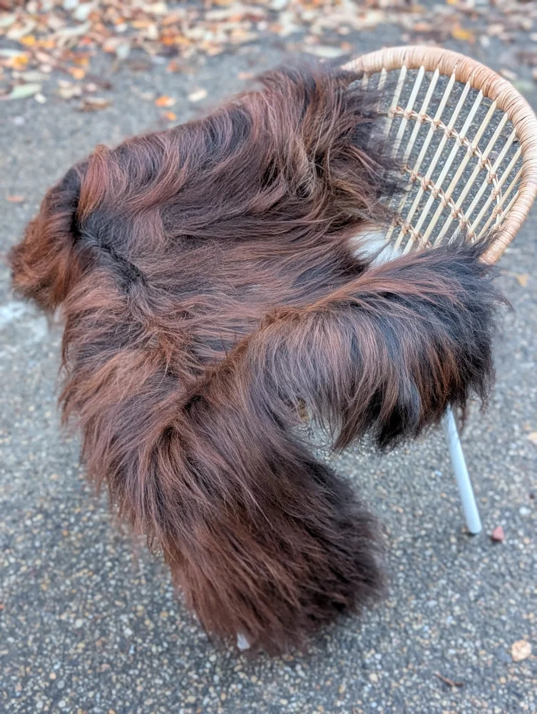 A thick dark rusty natural icelandic sheepskin throw draped over a wicker chair perfect for cozy decor