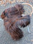 A thick dark rusty natural icelandic sheepskin throw draped over a wicker chair perfect for cozy decor