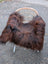 A cozy dark rusty icelandic sheepskin throw draped over a wicker chair with white metal legs perfect for snuggling