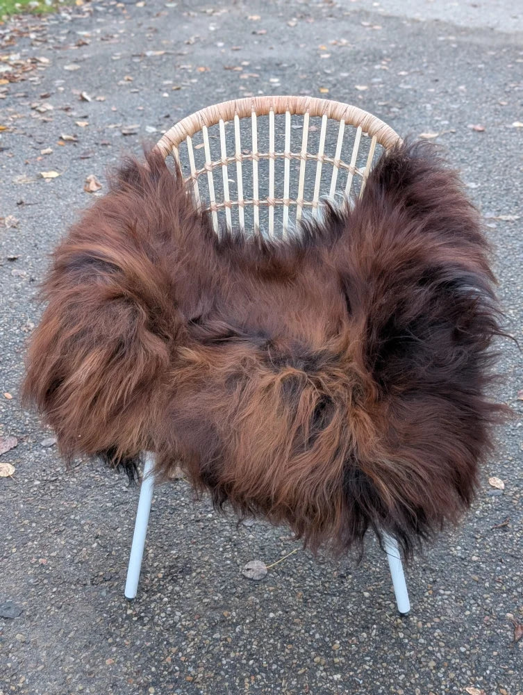 A cozy dark rusty long wool natural black icelandic sheepskin throw draped over a white rattan chair