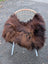 A cozy dark rusty long wool natural black icelandic sheepskin throw draped over a white rattan chair
