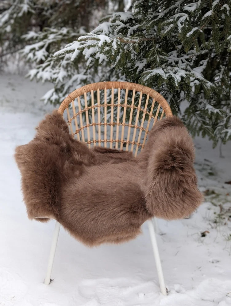 A cozy dark taupe merino sheepskin extra large blanket draped over a woven rattan chair with white metal legs