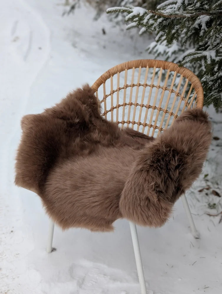 Dark taupe extra large merino sheepskin blanket draped over wicker chair showing soft texture and cozy feel