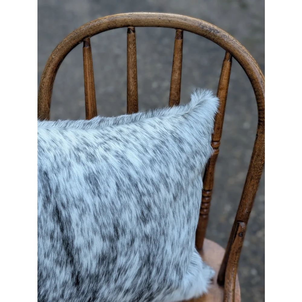 A plush double sided cowhide cushion mini moo double black steer head with light gray and black speckled texture on wood chair