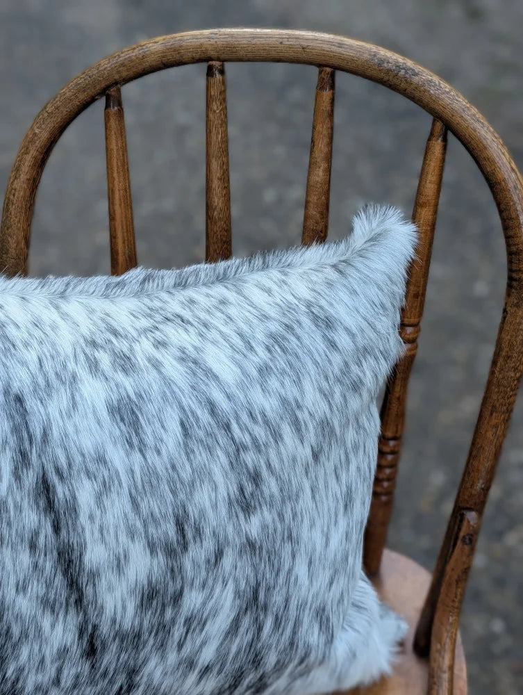 A plush double sided cowhide cushion mini moo double black steer head with light gray and black speckled texture on wood chair