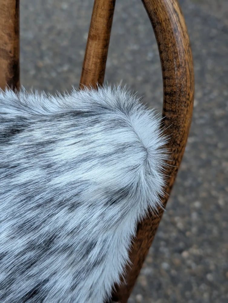 A plush gray and white speckled faux fur throw showing the back side of a double sided cowhide cushion mini moo double