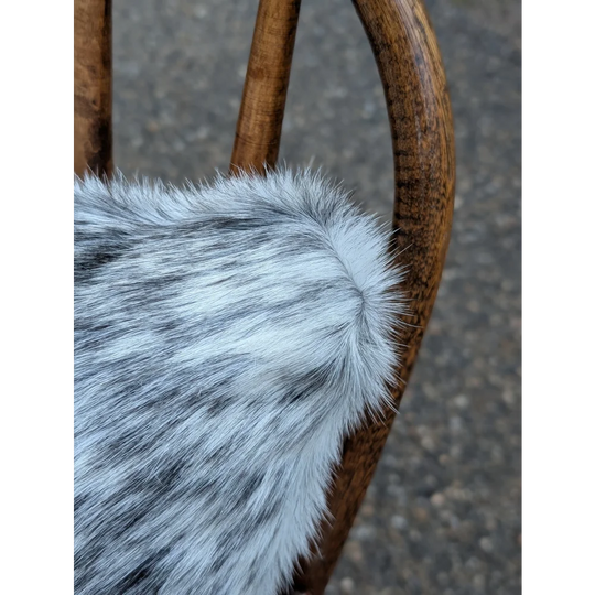 A plush gray and white speckled faux fur throw showing the back side of a double sided cowhide cushion mini moo double