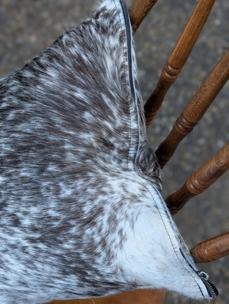 A plush gray and white double sided cowhide cushion mini moo with black zipper on speckled cowhide material