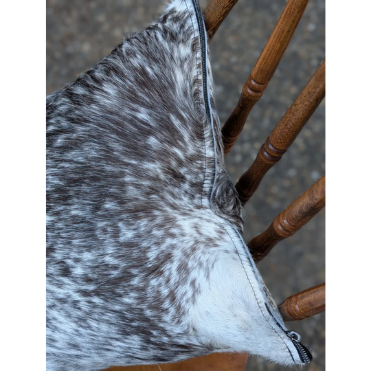 A plush gray and white double sided cowhide cushion mini moo with black zipper on speckled cowhide material