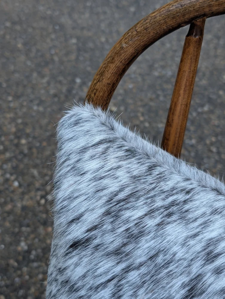 A plush gray and black speckled mini moo double sided cowhide cushion with a soft textured surface