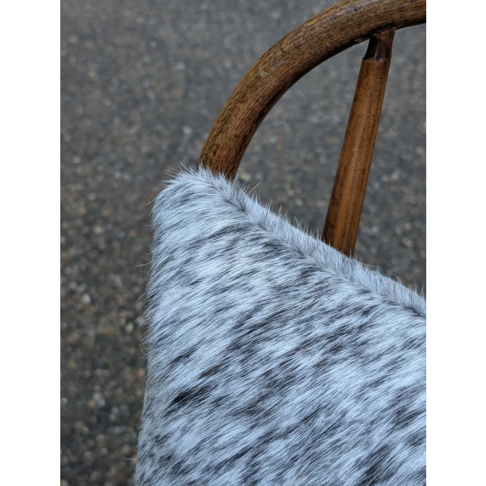 A plush gray and black speckled mini moo double sided cowhide cushion with a soft textured surface