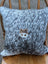 A cozy mini moo double sided cowhide cushion with gray and white speckled cowhide and a wooden cow face appliqué