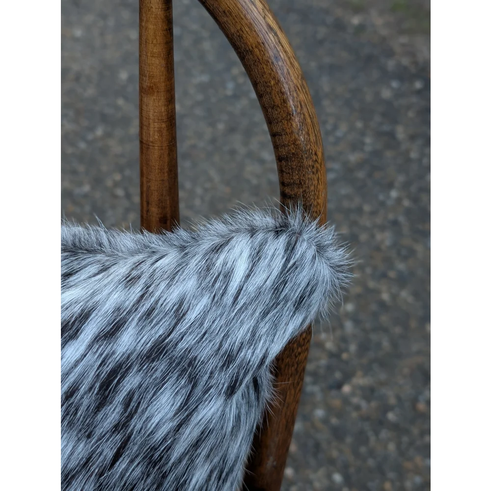 A plush gray and black faux fur throw draped over a wooden chair arm featuring mini moo double sided cowhide cushion