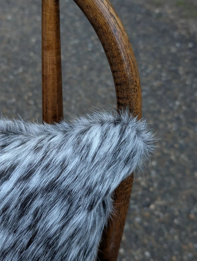A plush gray and black faux fur throw draped over a wooden chair arm featuring mini moo double sided cowhide cushion