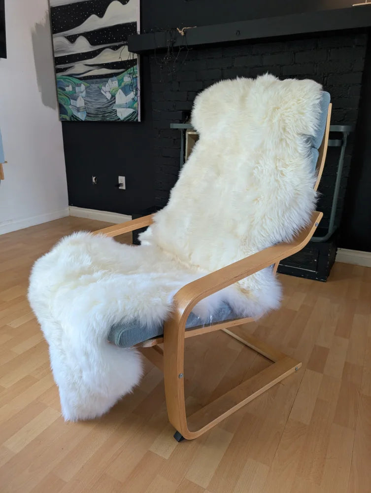 A cozy white double sheepskin throw oeko tex certified draped over a light wood lounge chair with gray cushions