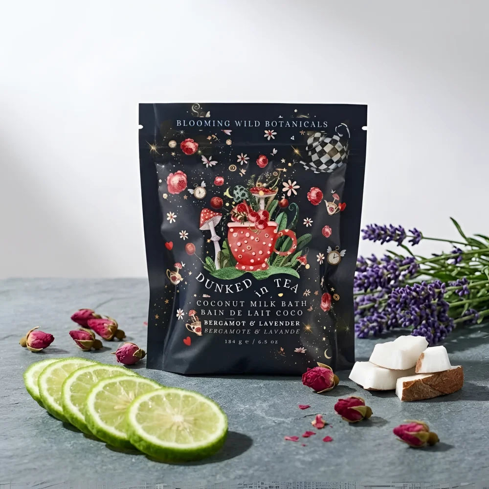 A dark blue pouch of angus oliver dunked in tea coconut milk bath with bergamot lavender surrounded by botanicals and lime slices
