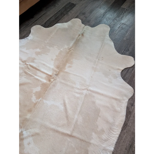 A large cream and white cowhide rug with natural irregular edges perfect for beautiful rugs collection