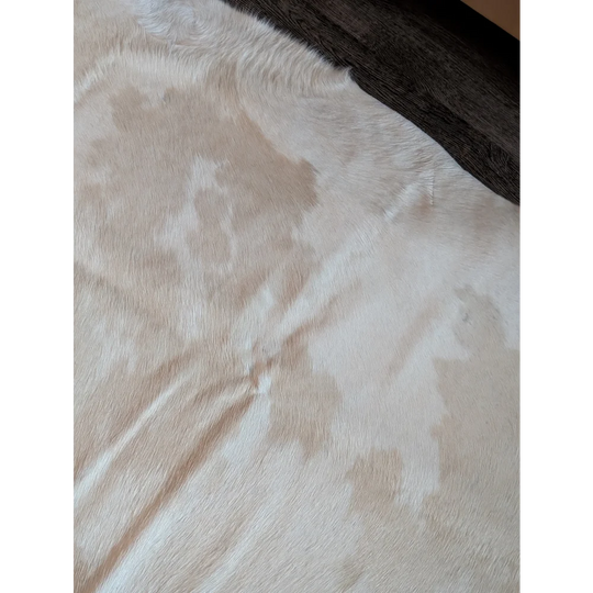 A beautiful large cowhide rug in white with natural tan patches and a soft textured furry surface perfect for decor