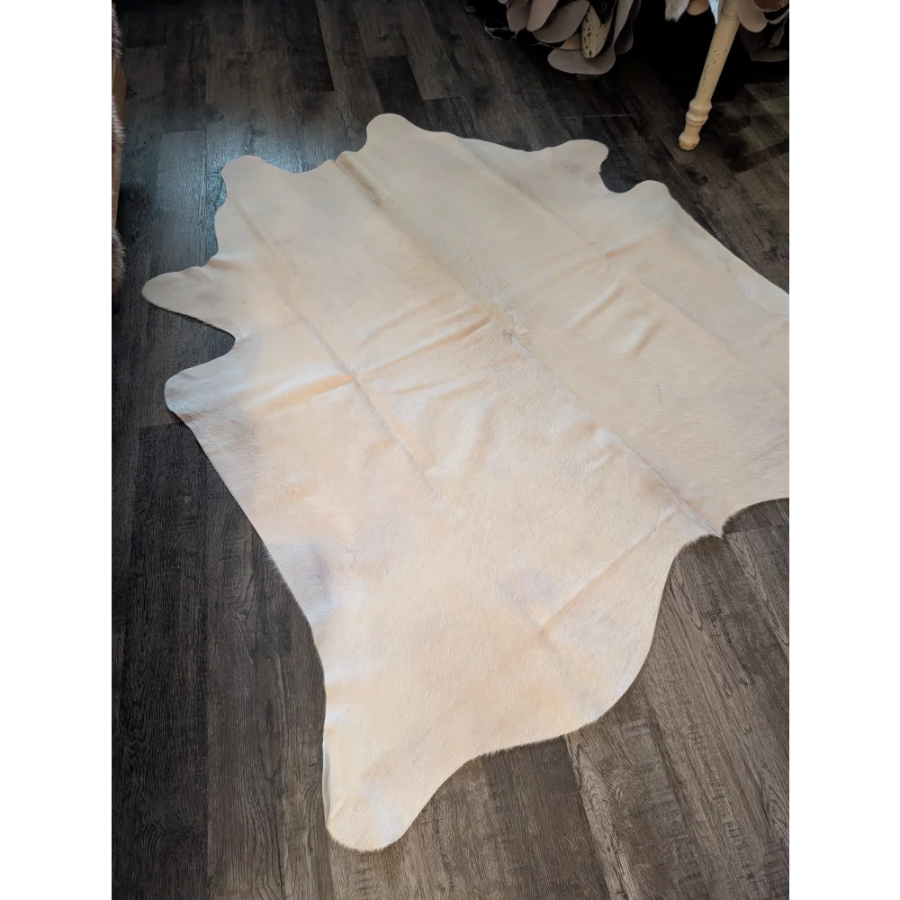 Cream-colored large cowhide rug with natural fur texture and irregular edges perfect for beautiful rugs