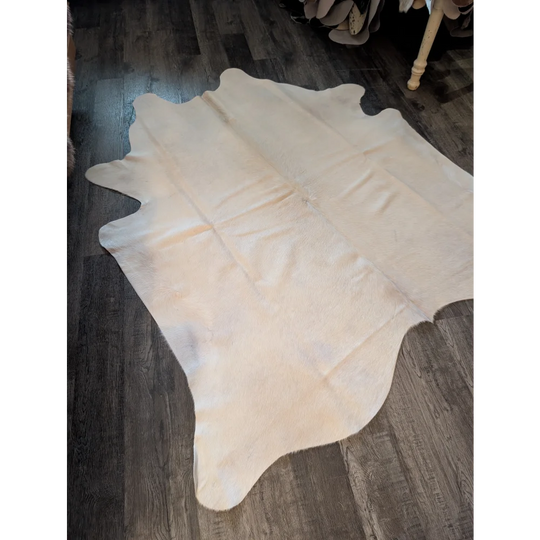 Cream-colored large cowhide rug with natural fur texture and irregular edges perfect for beautiful rugs