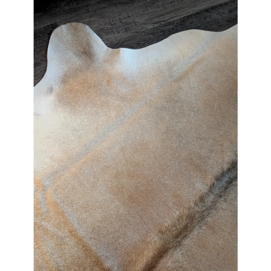 A large tan and white cowhide rug with a soft textured surface perfect for beautiful rugs and decor