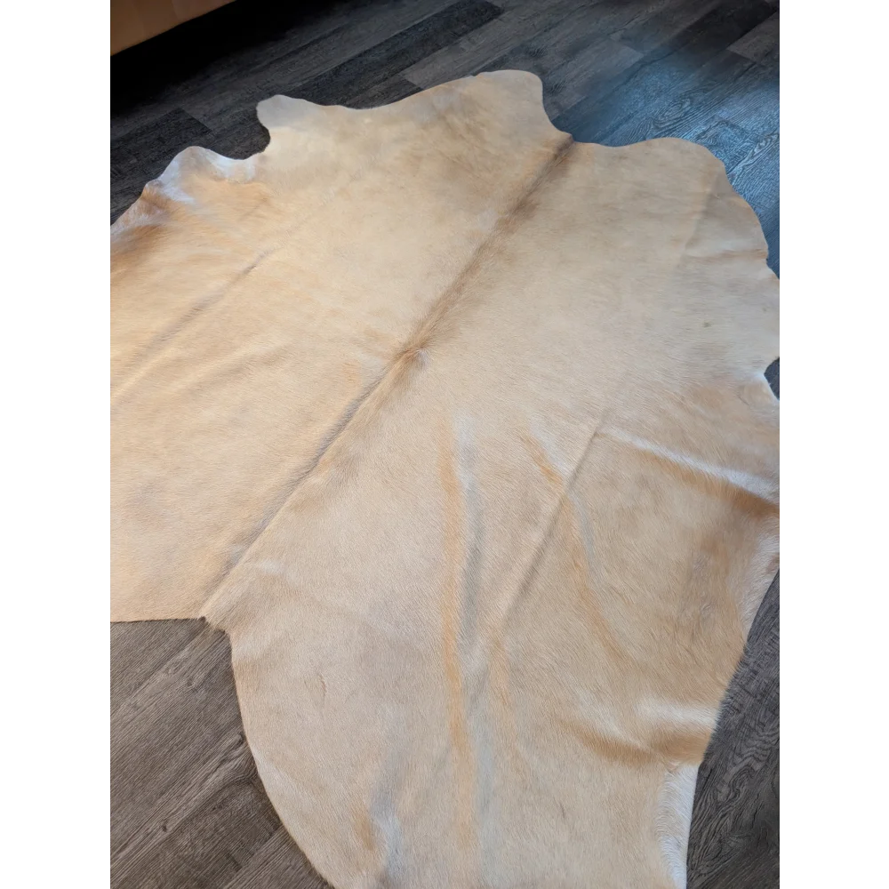 Cream-colored large cowhide rug with natural irregular edges and unique characteristics in a 73 by 73 inch size