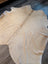 Cream-colored large cowhide rug with natural irregular edges and unique characteristics in a 73 by 73 inch size