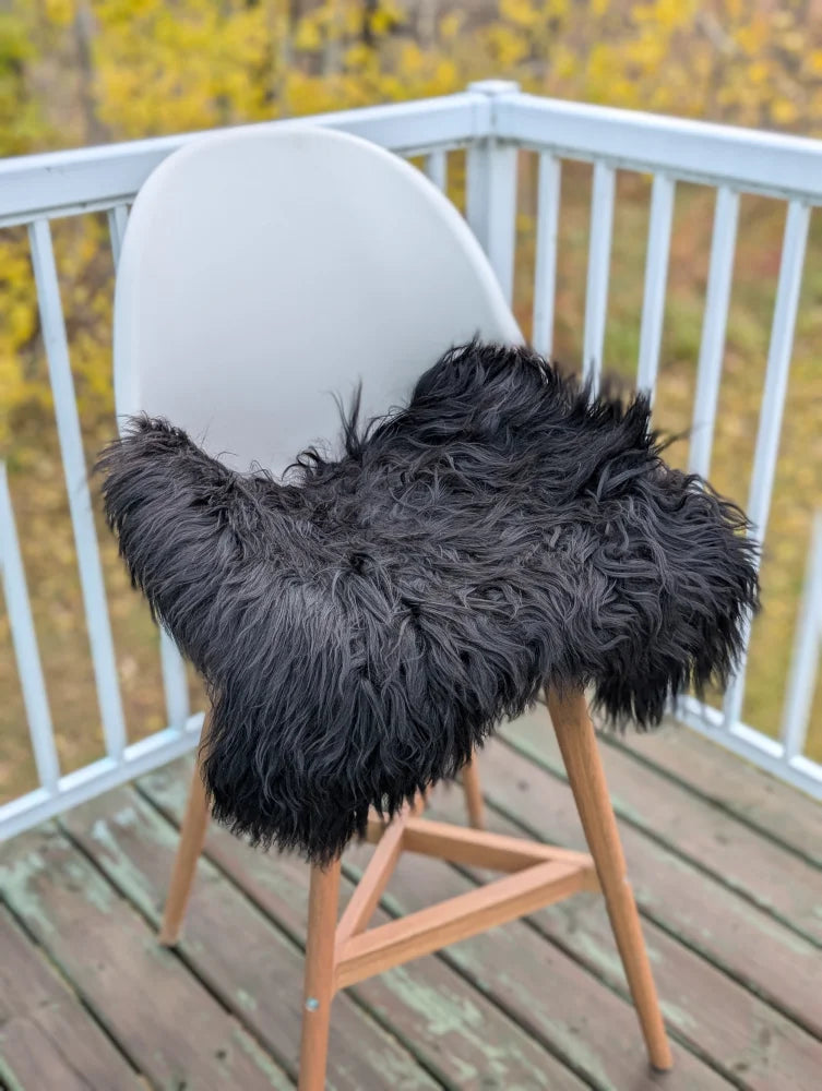 Black icelandic sheepskin chair cover draped over modern white chair with wooden legs extra large sheepskin chair pads
