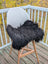 Black icelandic sheepskin chair cover draped over modern white chair with wooden legs extra large sheepskin chair pads