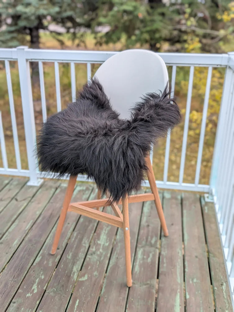 A sleek white chair with light wood legs draped in a plush black icelandic sheepskin for cozy seating