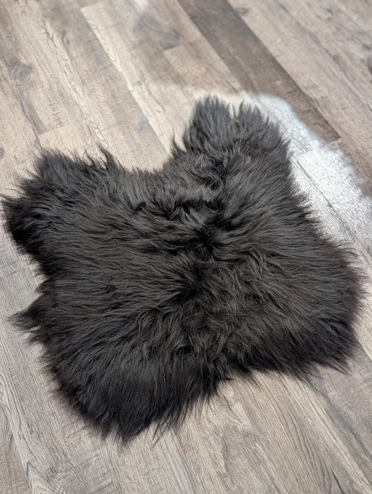 A plush extra large black icelandic sheepskin chair pad with soft fluffy texture lies flat on a wooden floor