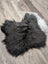 A plush extra large black icelandic sheepskin chair pad with soft fluffy texture lies flat on a wooden floor
