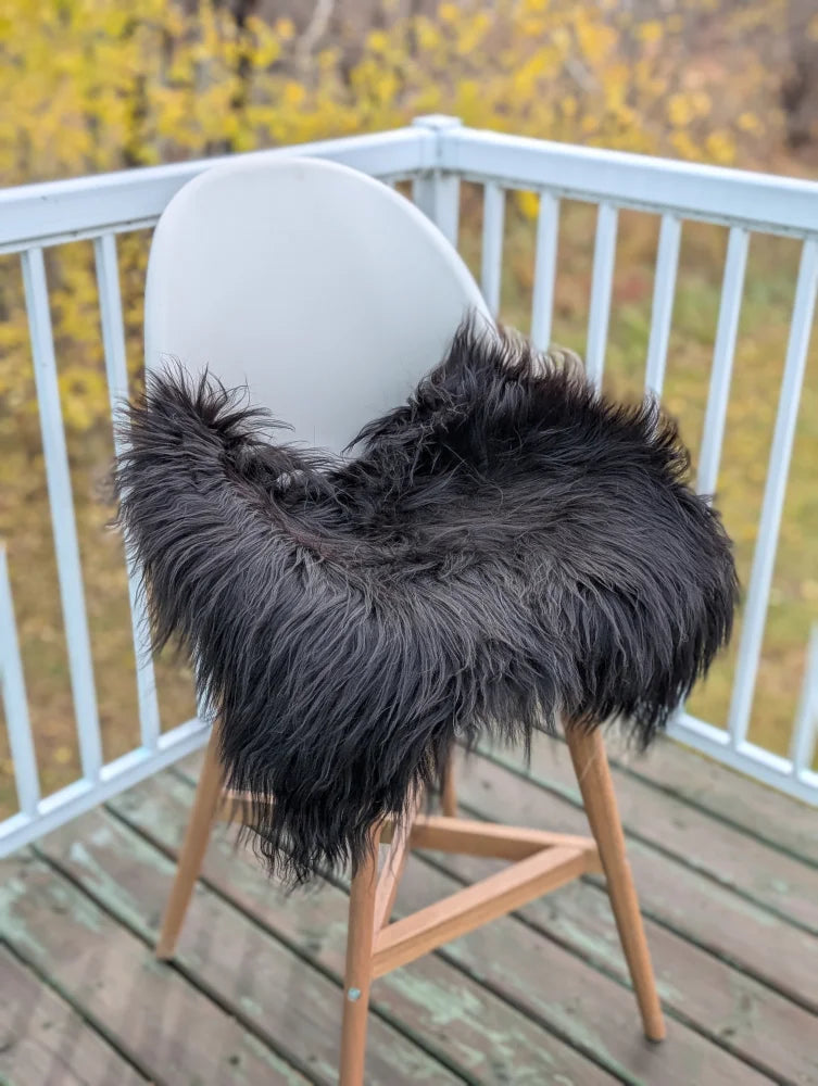 Black icelandic sheepskin chair pad draped over a modern white chair with wooden legs for cozy seating