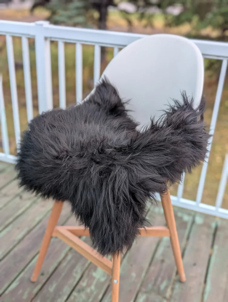 Black icelandic sheepskin chair throw draped over modern white chair with wooden legs perfect as extra large chair pads