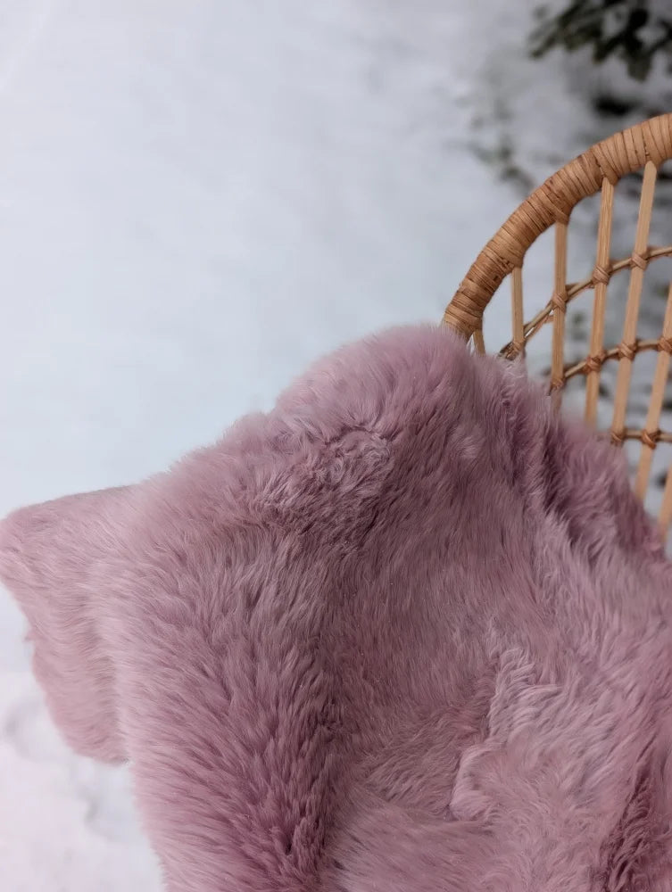A soft plush lavender pink merino sheepskin throw draped over a wicker chair meets reach standards