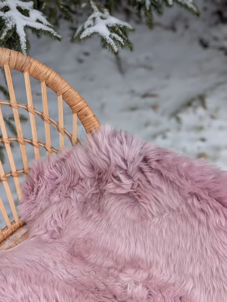A soft fluffy pink merino sheepskin throw draped over a woven wicker chair meeting reach standards
