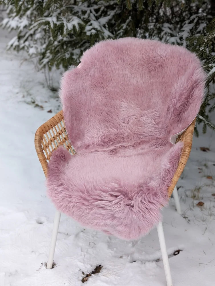 A soft fluffy pink merino sheepskin chair cover draped over a wicker outdoor chair meeting reach standards