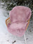 A soft fluffy pink merino sheepskin chair cover draped over a wicker outdoor chair meeting reach standards