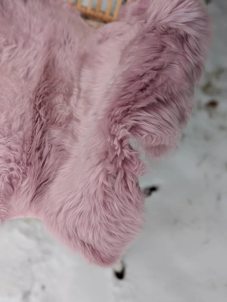 A soft fluffy pink merino sheepskin blanket with plush texture and slightly uneven edges perfect for cozy use