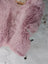 A soft fluffy pink merino sheepskin blanket with plush texture and slightly uneven edges perfect for cozy use